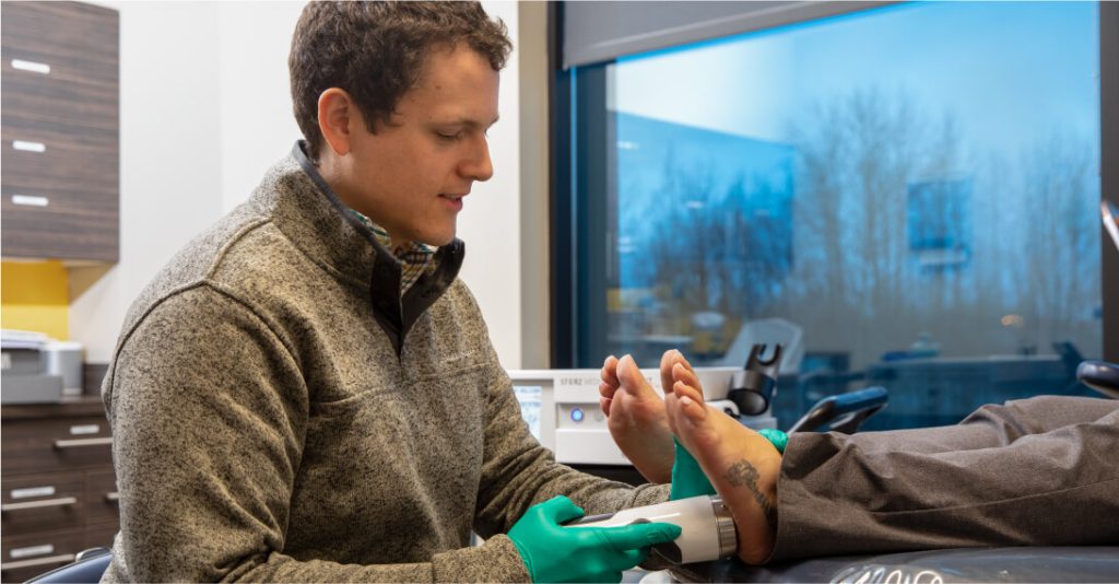 A doctor holds a medical tool up to a patient’s feet.